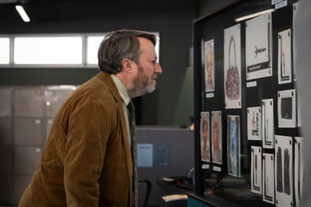 A man in a cord jacket and tie peers side on at a pinboard of images