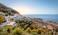 White washed houses on a hillside, with a blue sea and a blue sky in the background.