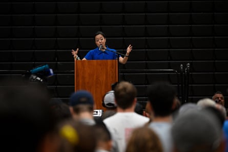 a woman standing at lectern with hands gestured while speaking to a crowd