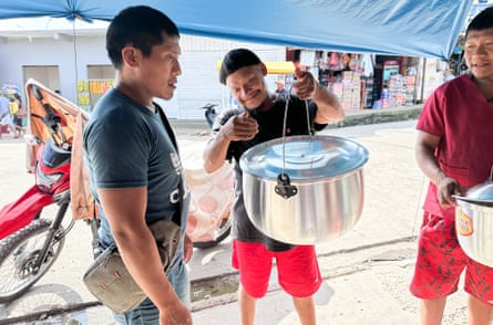 Three Indigenous men shopping for large cooking pots.