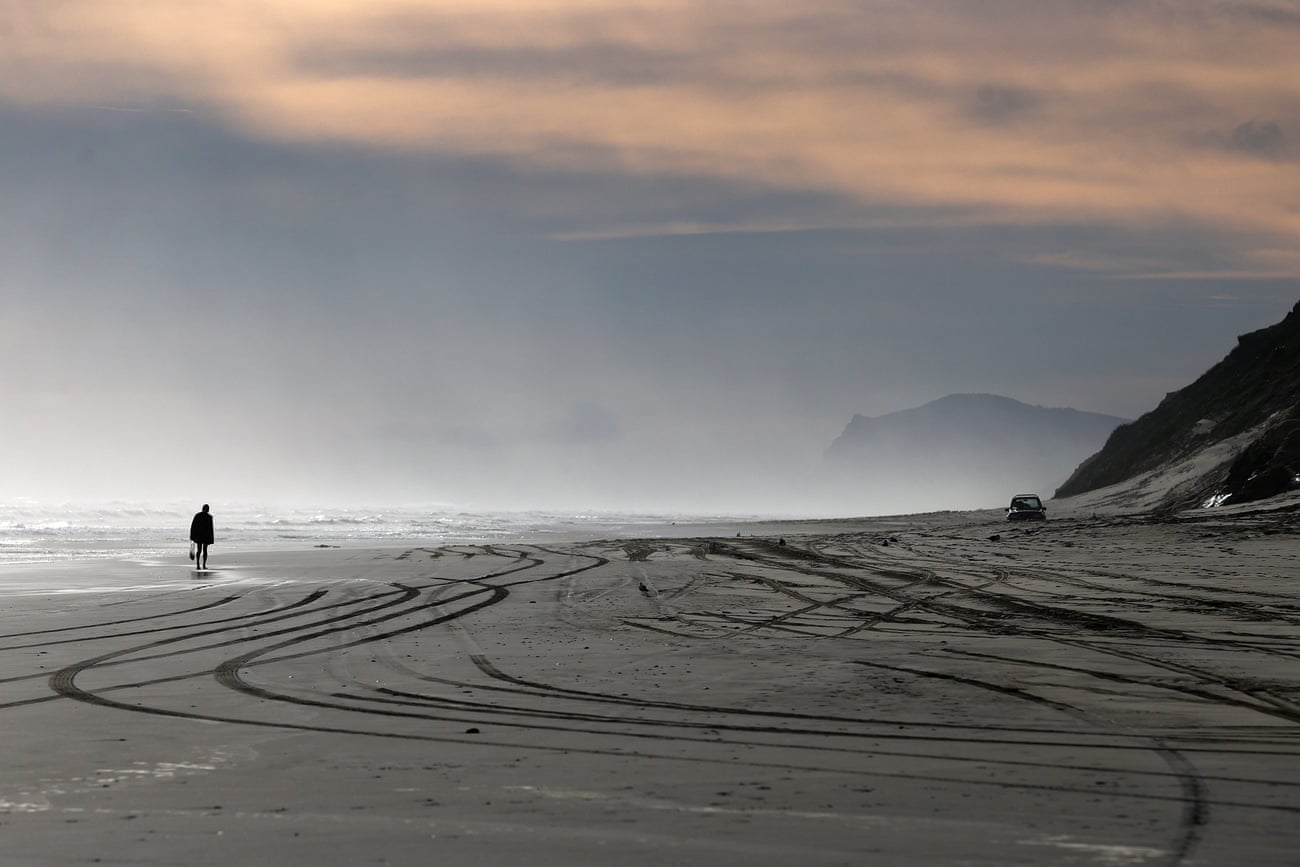 Wide view of a beach with multiple tracks in the sand and a person walking along the shore