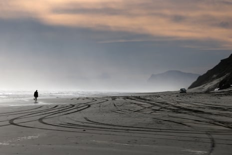 Wide view of a beach with multiple tracks in the sand and a person walking along the shore