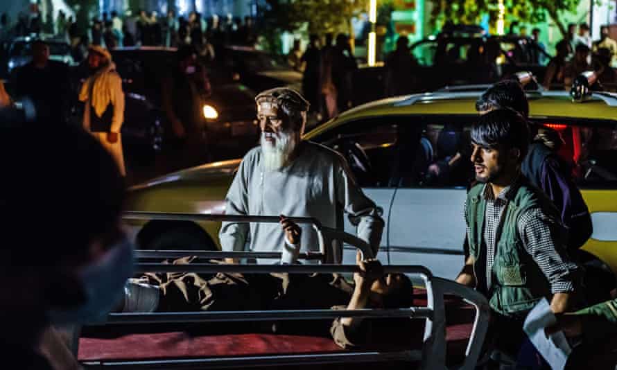 Two people push a stretcher with a wounded man through a crowded street scene at night