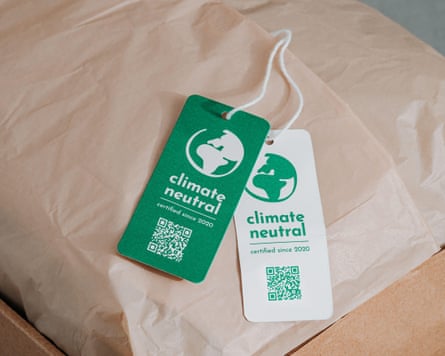 Green and white labels reading ‘climate neutral: certified since 2020’ lie on a brown paper-wrapped parcel in a cardboard box