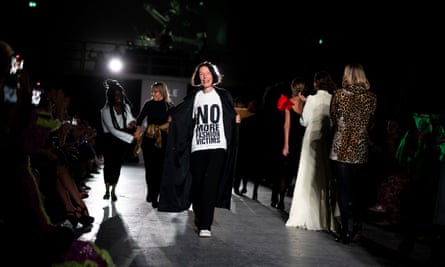 Woman on catwalk wearing black trousers and black coat with a white t-shirt with slogan 'no more fashion victims'