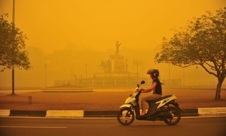 A woman rides a motorbike amid thick yellow haze caused by raging forest fires in Indonesia.
