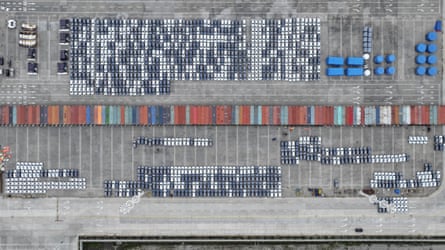 An aerial image of electric vehicles being loaded into containers at a port