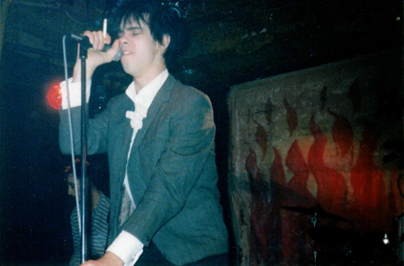 A young Nick Cave sings on stage with a cigarette in his hand
