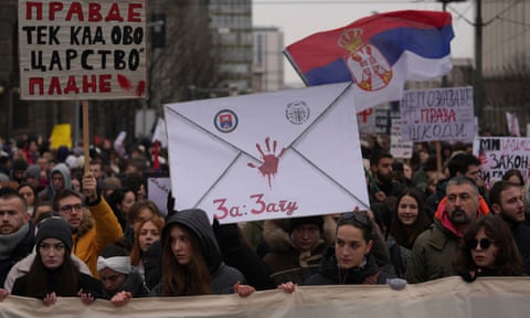 A crowd of people carrying placards and waving the Serbian flag march in Belgrade qhiukiqrihdinv