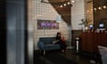 A person scrolls on their phone while sitting on a couch underneath a neon sign reading 'WeWork.'