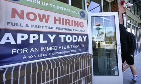 A man walks into a restaurant displaying a "Now Hiring" sign