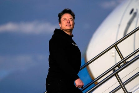 Elon Musk in a black hoodie walking up a staircase on to the Air Force One plane