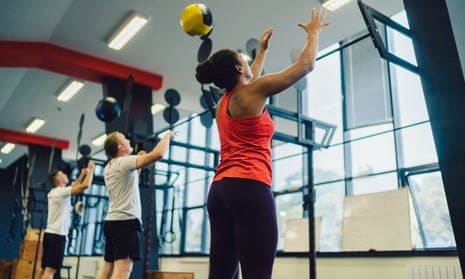 One woman and two men exercise in a gym and do squats using sports balls