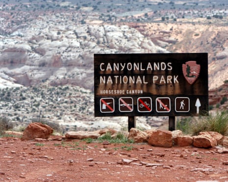 Canyonlands National Park sign with warning icons stands amid rocks overlooking Utah's canyon badlands