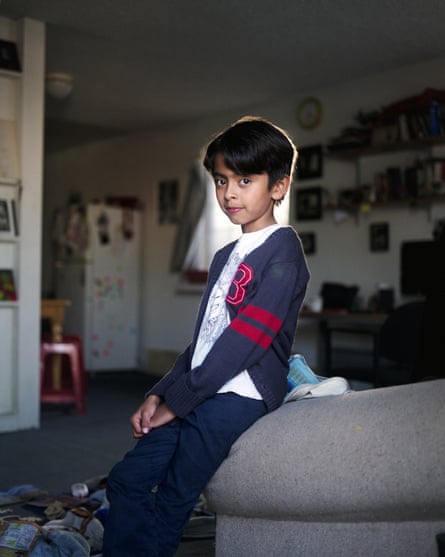 A young boy sitting on the arm of sofa cast in light from a window behind him