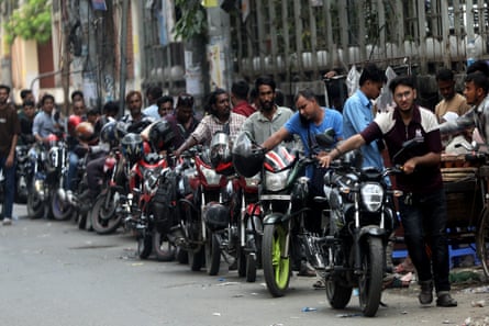 A long line of men pushing motorbikes along a road
