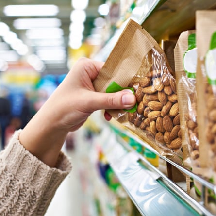 A hand takes a packet of skin-on almonds from the shop shelf