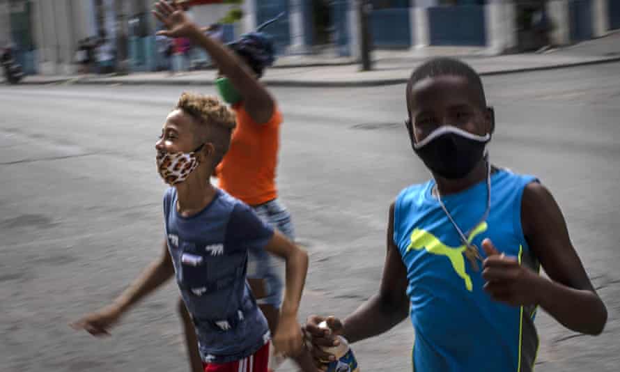 Niños con máscaras de precaución en medio de la propagación de un nuevo virus corona que corre por una calle de La Habana.