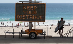 A surfer walks back from the beach past social distancing signage at Scarborough Beach in Perth