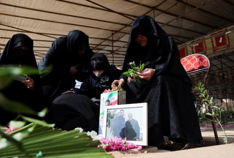 Women in all black and black hijabs lay flowers next to a photo of someone killed in a US-Israeli airstrike in Iran.