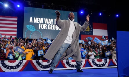 Man in long gray trench coat on stage.