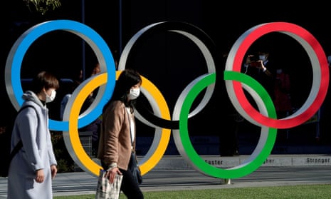 Women wearing protective face masks walk past the Olympic rings in Tokyo.