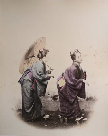 Two women in traditional Japanese kimono stand back to back, one holding a parasol