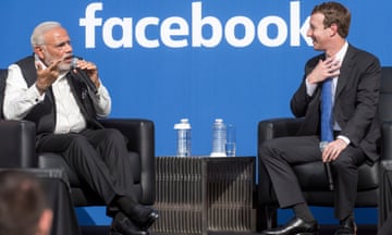Narendra Modi holds a microphone as he speaks to Mark Zuckerberg while seated on stage