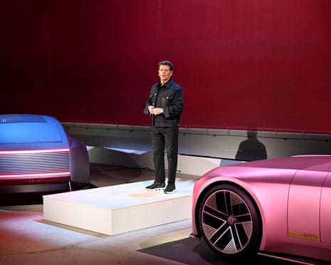 Gerry McGovern standing on stage between pink and blue Jaguars