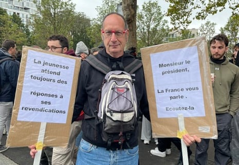 Pierre holding up two cardboard messages reading: “The young people are waiting for responses to their demands” and “Mr. President, France is speaking to you, listen to us”