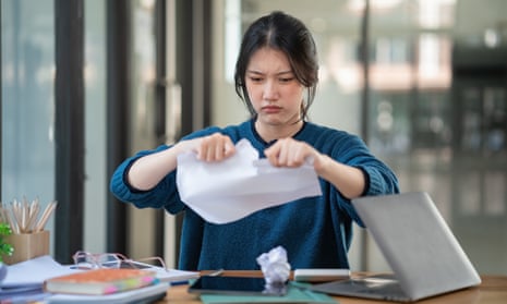 A young woman tearing up paperwork at a desk in an office.