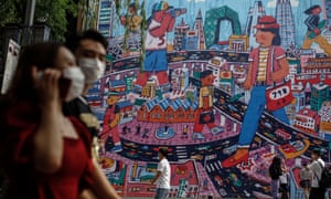 People wearing protective face masks walk by a giant painting depicting the capital city amid coronavirus pandemic at 798 art zone in Beijing, China, 26 June 2020.