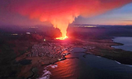 An aerial shot of a coastal town with smoke rising from an area of molten orange lava