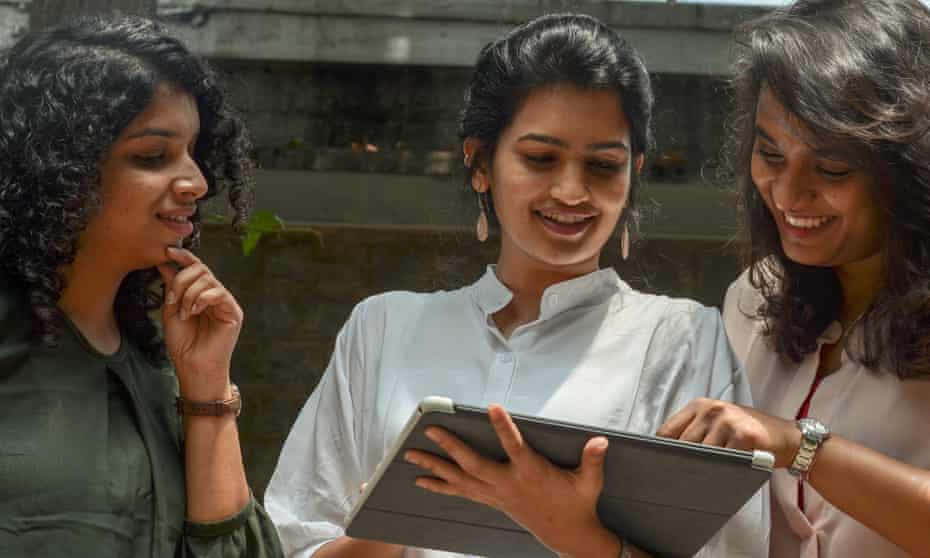 Three young smiling women working outdoors on mobile device