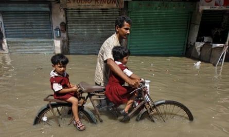A man takes his daughters home from school on a bicycle through a flooded road in Kolkata.