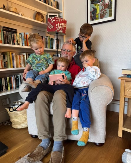Martin Roach with his grandchildren, sitting on a chair showing them something on a phone