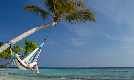 A young man is having a nap in a hammock over the sea.