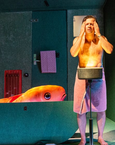 a man stands at a bathroom sink holding his head in his hands while a giant goldfish swims in the bath next to him, in a scene from the show "I… er… Me" at the Edinburgh international children’s festival