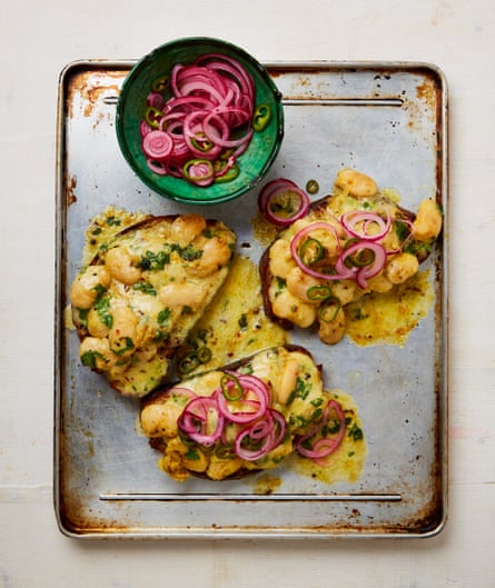 Cheesy curried butter beans on toast on a metal tray with a bowl of red onion