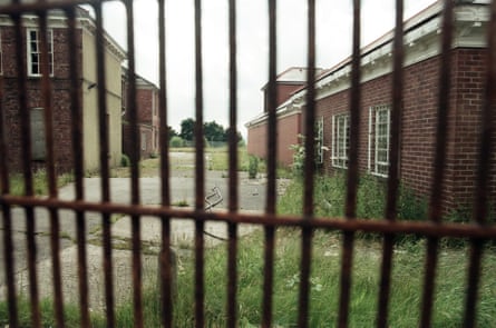 Dilapidated brick buildings seen through an iron fence