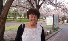 Pnina Werbner, in a white crochet top, stands smiling in front of a flowering cherry tree in a park