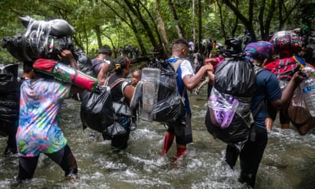 A group of men, women and children support each other as they wade across a fast-flowing river with their possessions in plastic bin bags