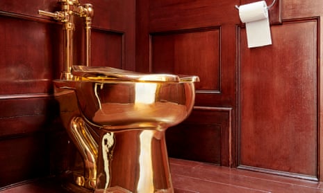 A gold toilet in a wood-panelled room with a toilet roll hanging on the wall