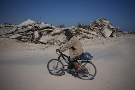 A Palestinian man cycling past the rubble of buildings destroyed by Israeli strikes in Khan Younis, Gaza.