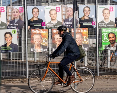 A person cycles past election posters attached to a metal fence
