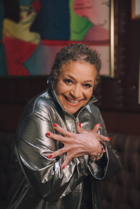 Wearing a silver jacket and smiling, Debbie Allen clutches her chest dramatically