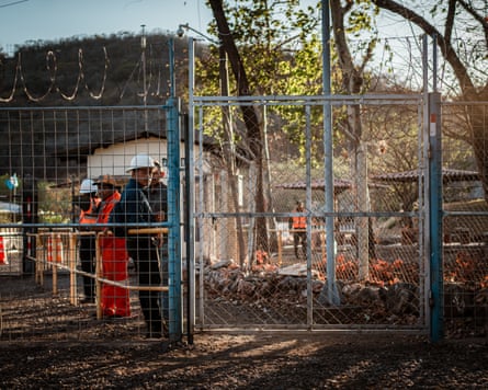 A small group of men, some wearing hard hats, behind a fence and gate with barbed wire on top