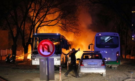 A police officer gestures as he walks at the site of an explosion while firefighters try to extinguish flames after an attack targeted a convoy of military service vehicles in Ankara
