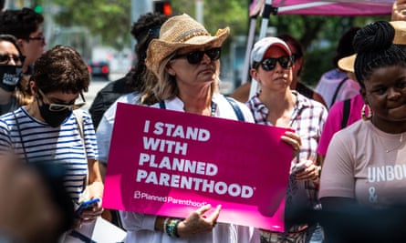 woman holds sign saying 'i stand with planned parenthood', surrounded by other protesters