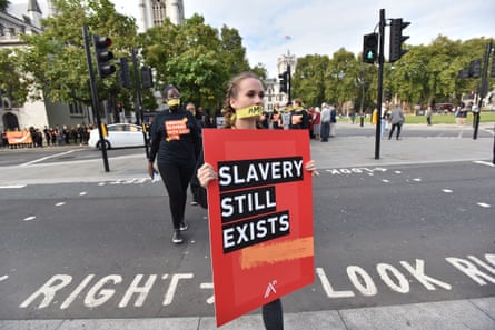People march in London against modern slavery wearing masks. One young woman holds a placard that says 'slavery still exists'.